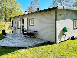A single-story house with a deck, a small outdoor table, and a green lawn. - 4 Star Holiday Home in Solvesborg (Sölvesborg)