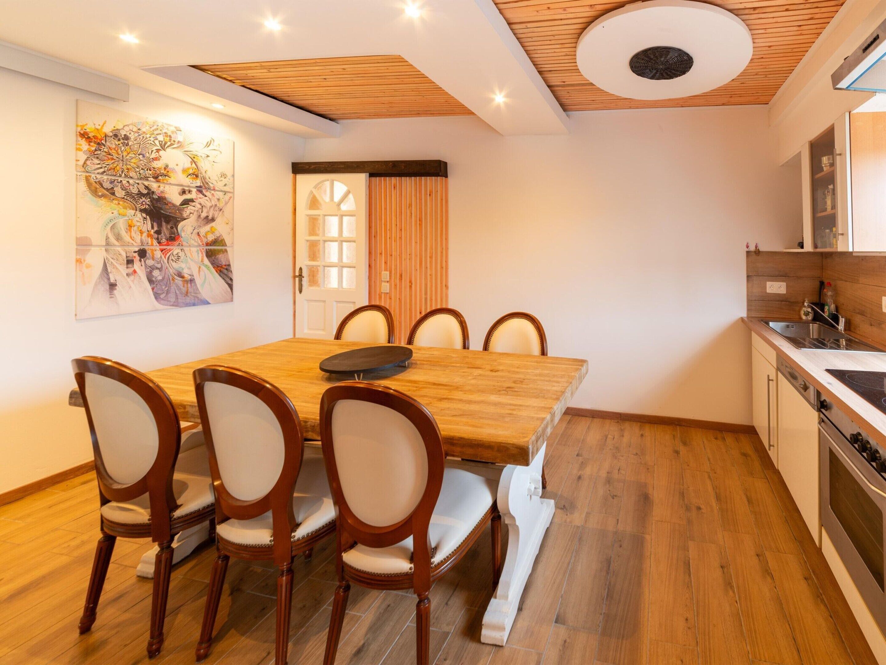 Une cuisine moderne avec une table et des chaises en bois, un coin repas agrémenté d’un tableau, et un plafond en bois.