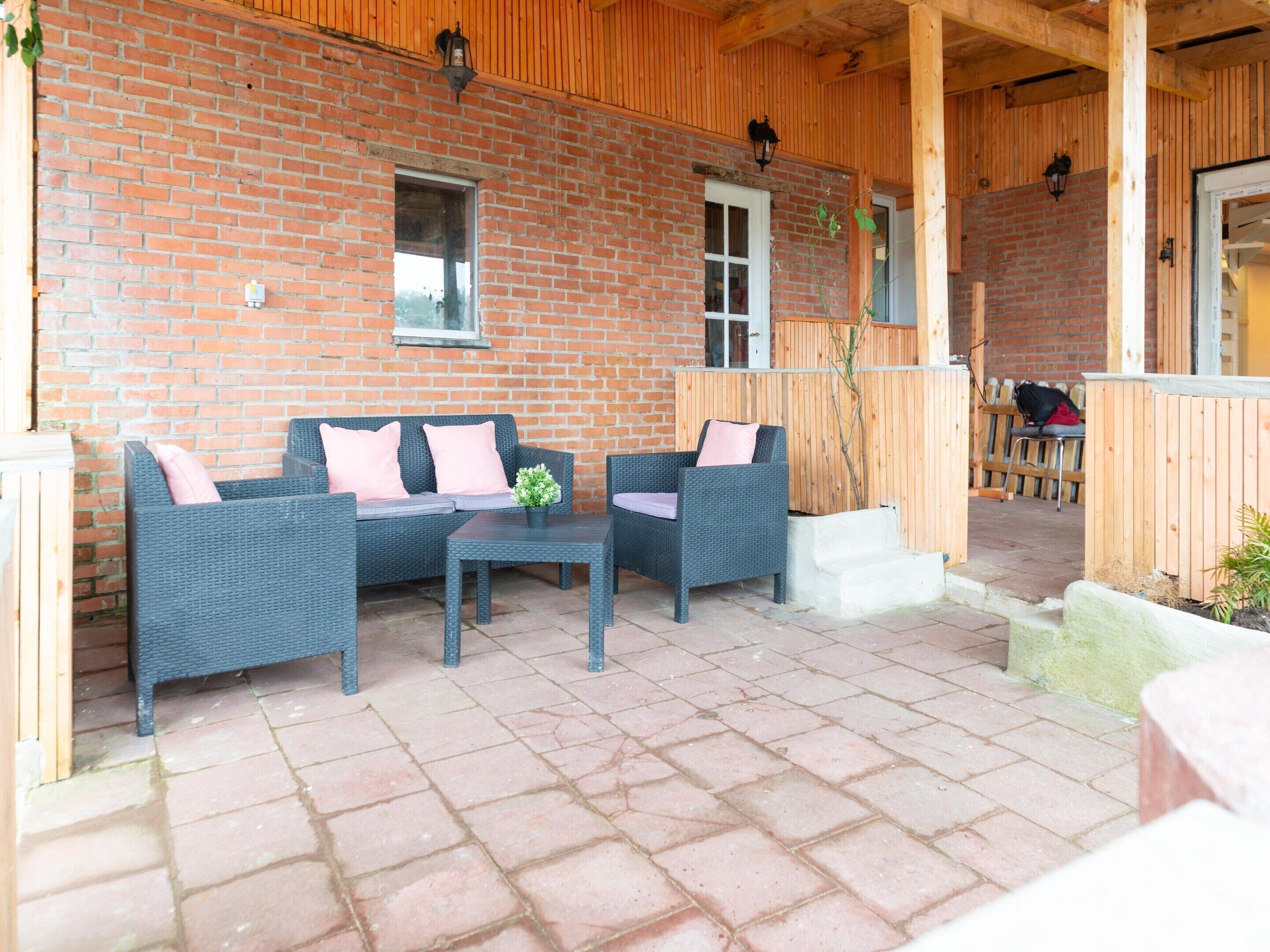 An outdoor patio with wicker furniture, a brick wall, and wooden beams.