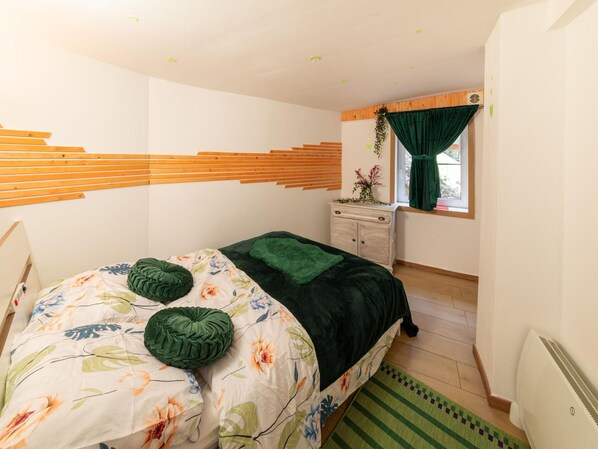 Une chambre à coucher avec un lit, une commode, une fenêtre avec des rideaux et un radiateur.