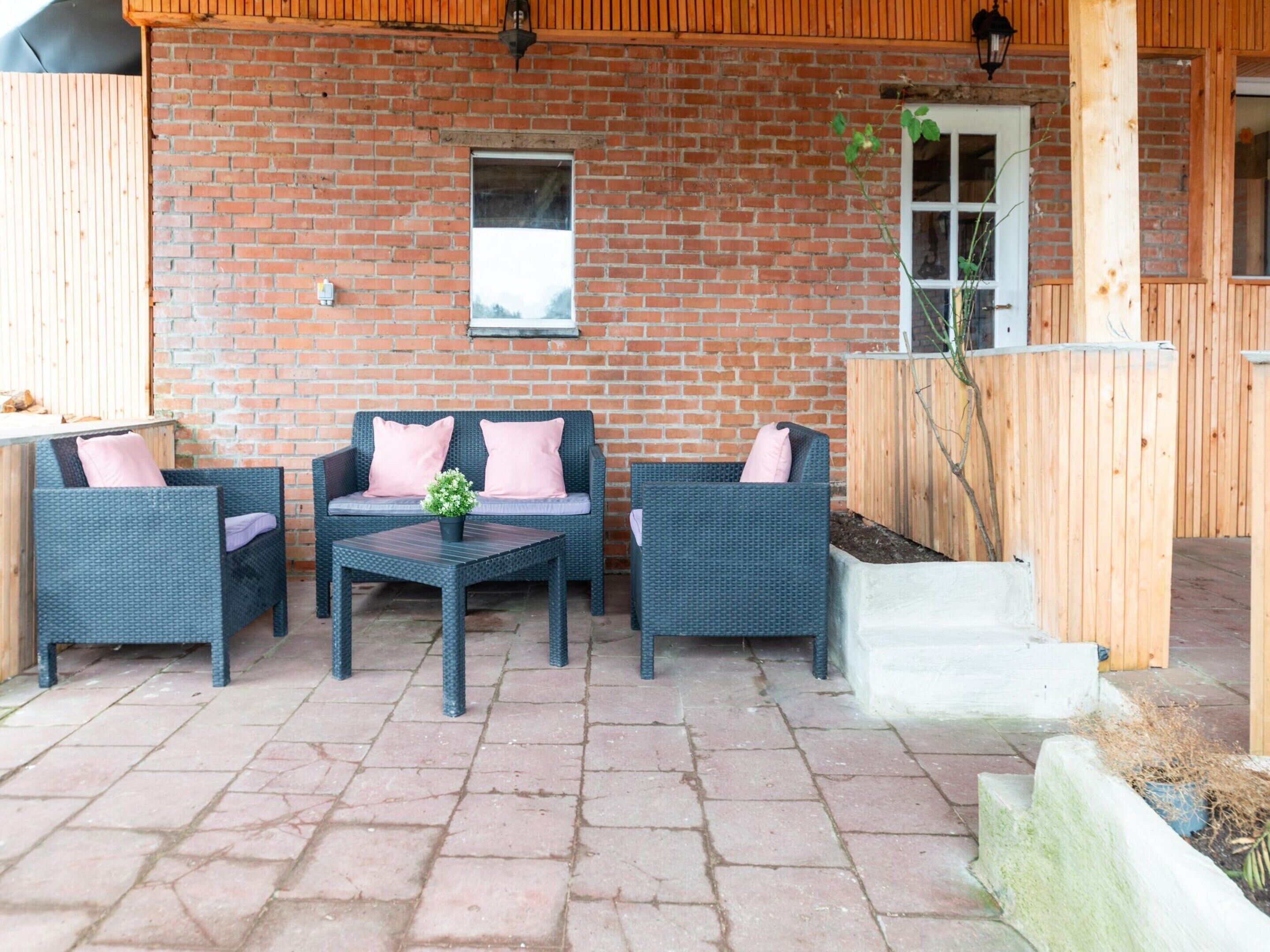 An outdoor patio with wicker furniture, a brick wall, and a wooden fence.