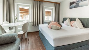 A modern hotel room with a bed, a desk, and a chair. There are two windows with curtains, a painting on the wall, and a wooden ceiling. - Nice Apartment in Sautens With a Cozy Terrace (Sautens)