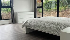 Un dormitorio moderno con una cama grande, un televisor montado en la pared y vistas al exterior a través de amplias ventanas.