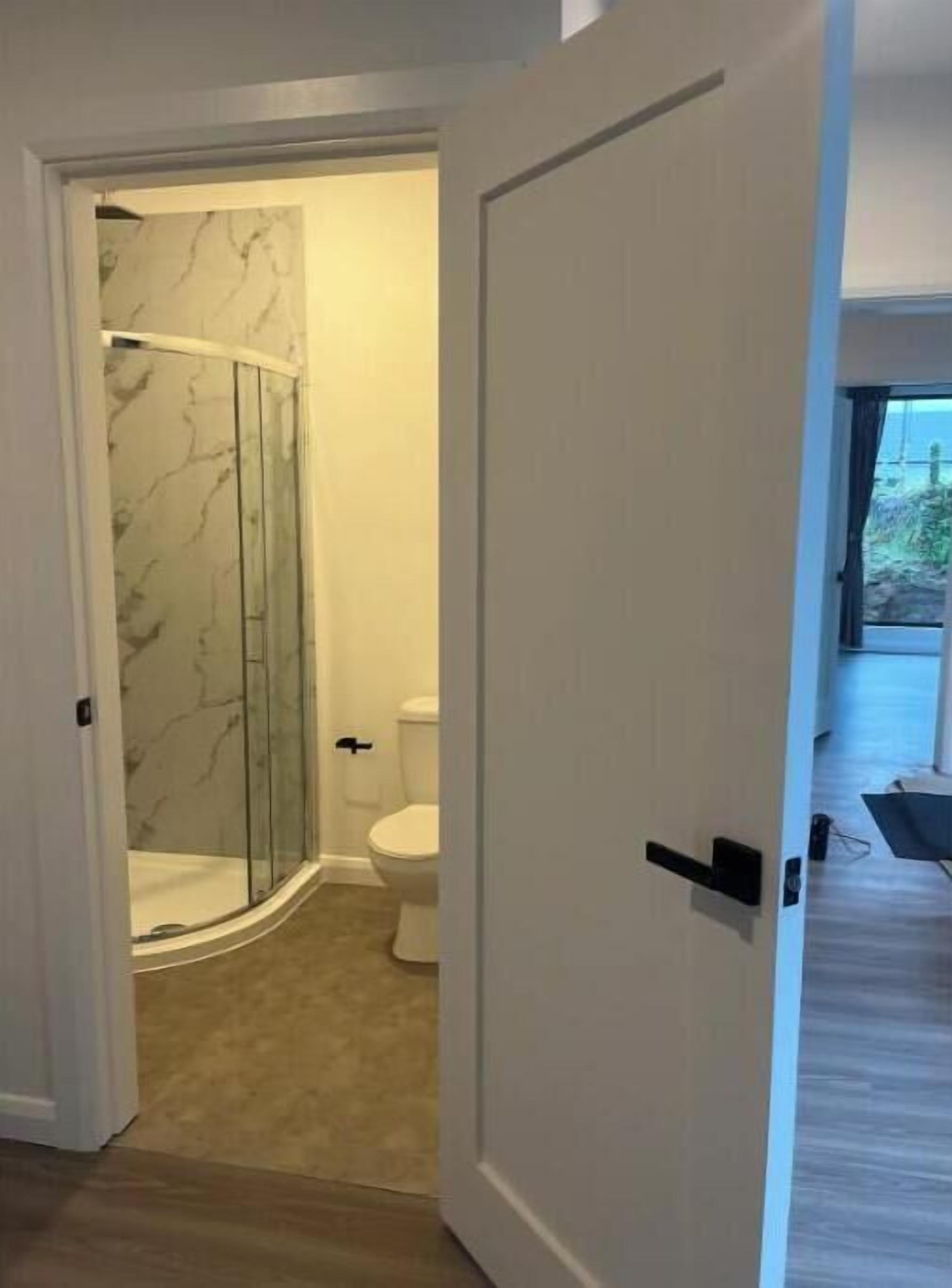 Ein Badezimmer mit Duschkabine aus Glas, Toilette und einem beigefarbenen Teppich.