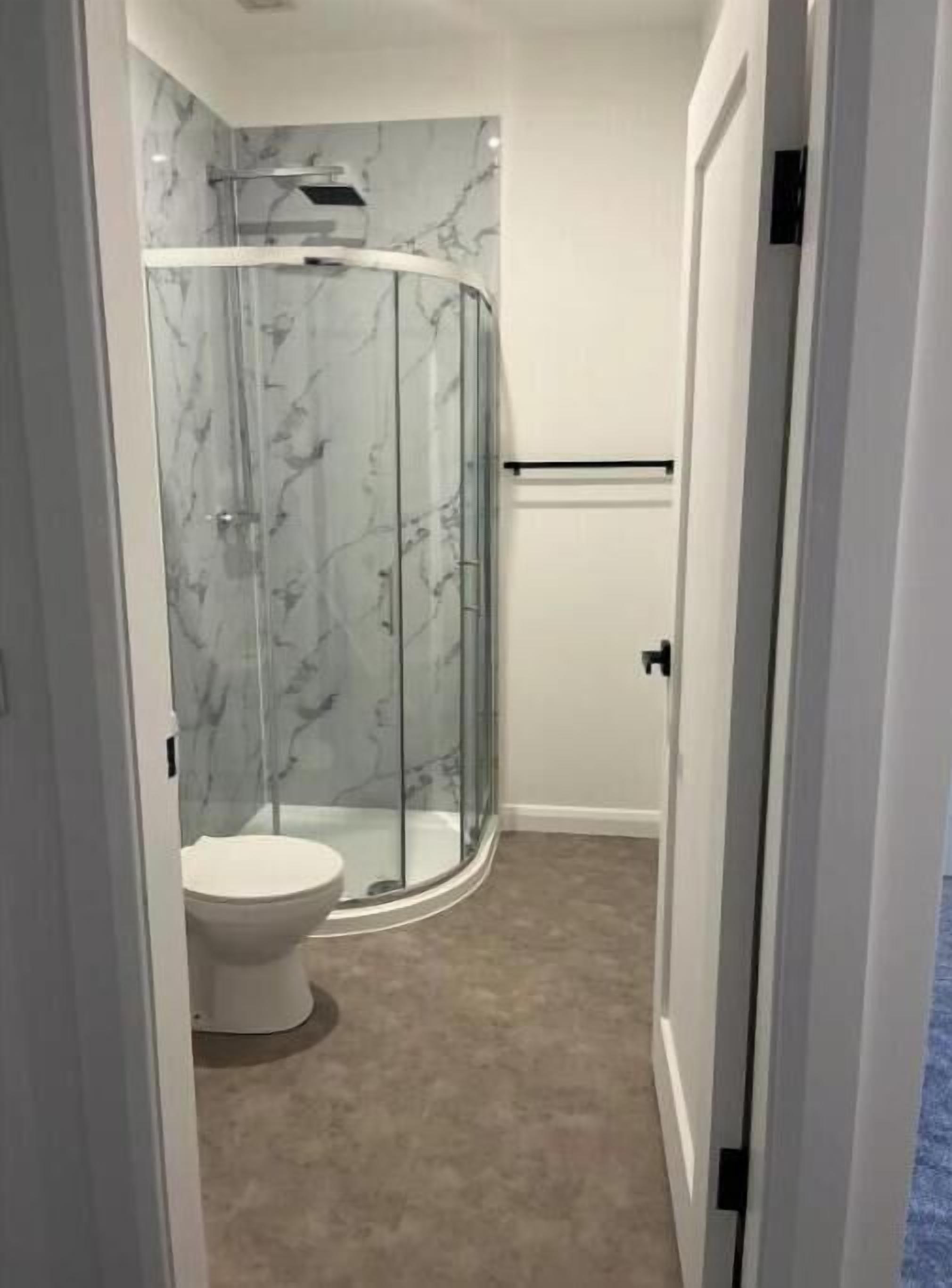 Un baño con cabina de ducha de vidrio, inodoro y paredes con estampado de mármol.