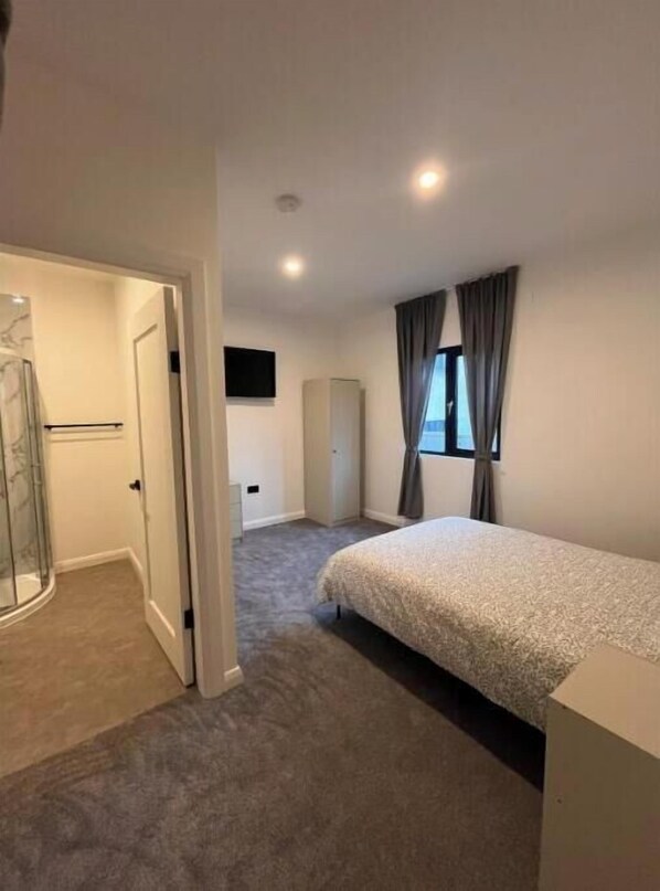 Une chambre avec un lit, une douche, une armoire et un téléviseur fixé au mur.