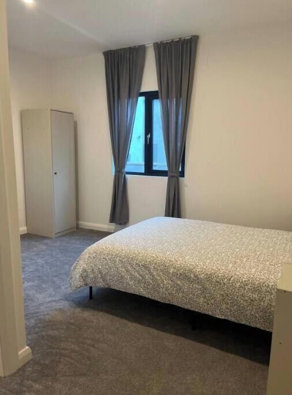 A bedroom with a bed, a wardrobe, and a window with curtains.