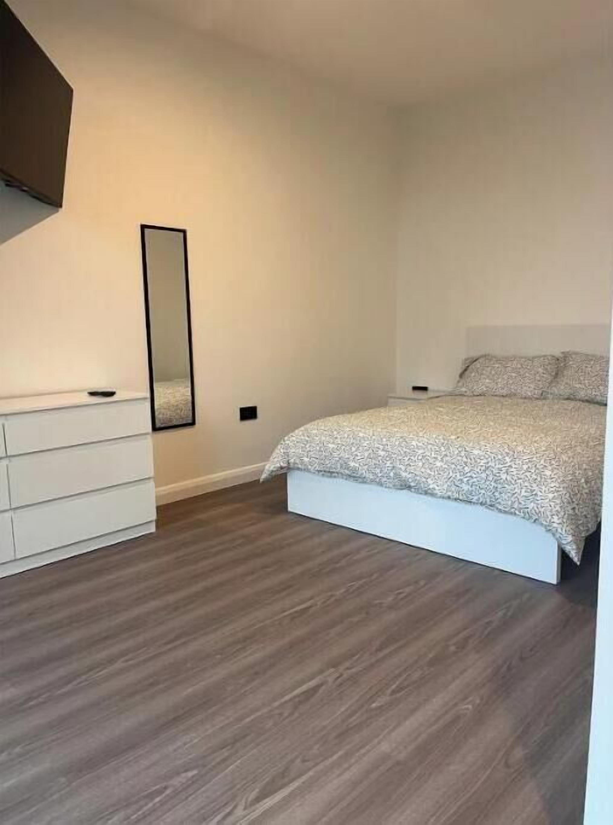 Een slaapkamer met een bed, een ladekast, een spiegel en een lichtschakelaar aan de muur.