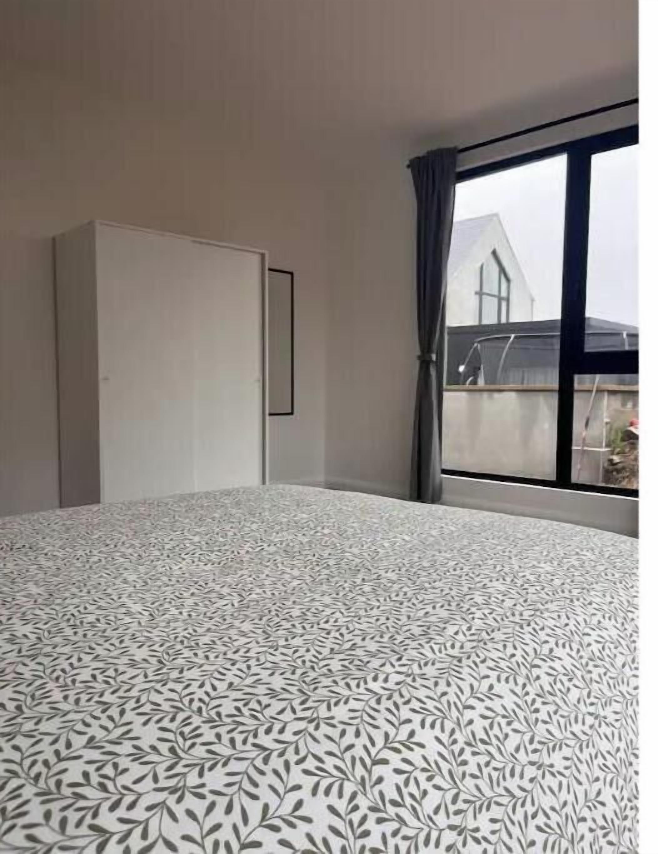 A hotel room with a bed, a wardrobe, a window with a view of a building, and a curtain.