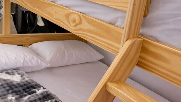 Un lit superposé avec une structure en bois, une literie blanche et une couverture pliée sur le lit du bas.