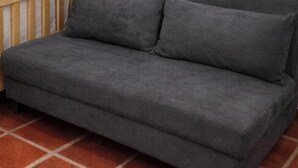Un canapé gris, recouvert d’un tissu texturé, est placé sur un sol carrelé.