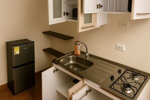 Une cuisine de taille réduite, dotée d’un réfrigérateur noir, d’un évier en acier inoxydable et d’une cuisinière à gaz.