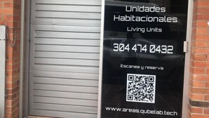 Une devanture de magasin avec un volet métallique fermé, un code QR et un texte indiquant « Unidades Habitacionales Living Units », ainsi qu’un numéro de téléphone et une adresse de site web.