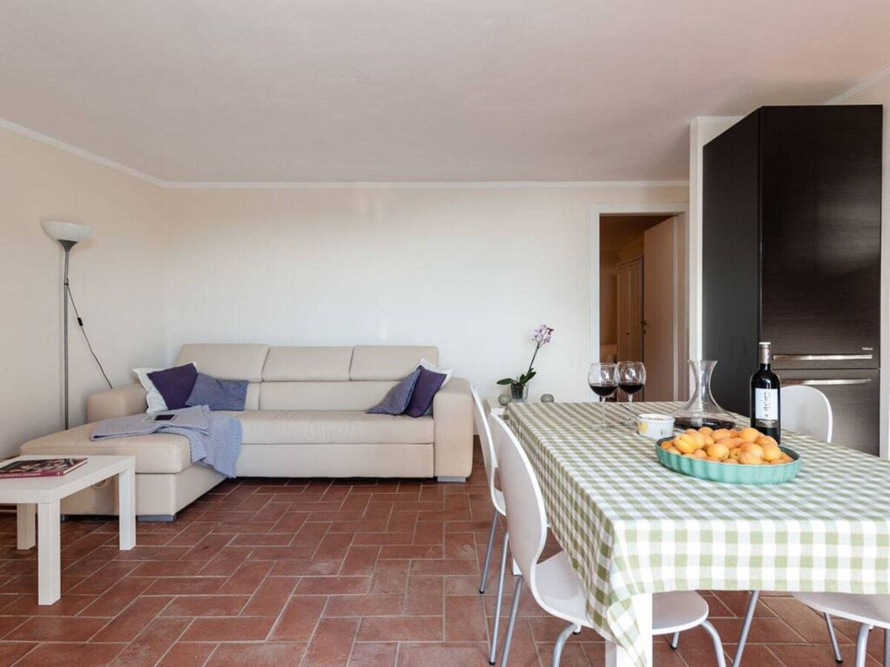 A living room with a sofa, a dining table with a checkered tablecloth, and a kitchen area with a refrigerator.