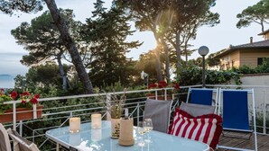 A deck with a glass table, chairs, and a view of the sea. - Casina di Savolano Comfortable Holiday Residence (Livorno)