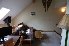 A cozy room with a sloped ceiling, a wooden bench, a sofa with cushions, a framed picture on the wall, and a lamp.