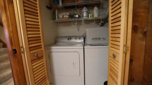 A laundry room with a washing machine and dryer, wooden doors, and a shelf with cleaning supplies. - Relax at This Mountain View Condo in the Estates! (Campton)