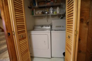 A laundry room with a washing machine and dryer, wooden doors, and a shelf with cleaning supplies.