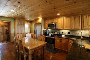 Una cocina de madera con una mesa de comedor, sillas, un refrigerador, un microondas, un horno y un lavaplatos.