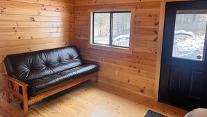 A wooden cabin interior with a leather sofa, wooden walls, and a door leading outside. - Lake Carey Cabin within walking distance to Old Carter Barn with lake access (Tunkhannock)