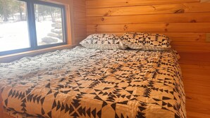 A wooden cabin room with a bed, a window, and a view of trees and rocks outside. - Lake Carey Cabin within walking distance to Old Carter Barn with lake access (Tunkhannock)