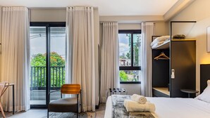 Ein Hotelzimmer mit Bett, Sessel, kleinem Tisch, Kleiderschrank und Blick durch ein großes Fenster.