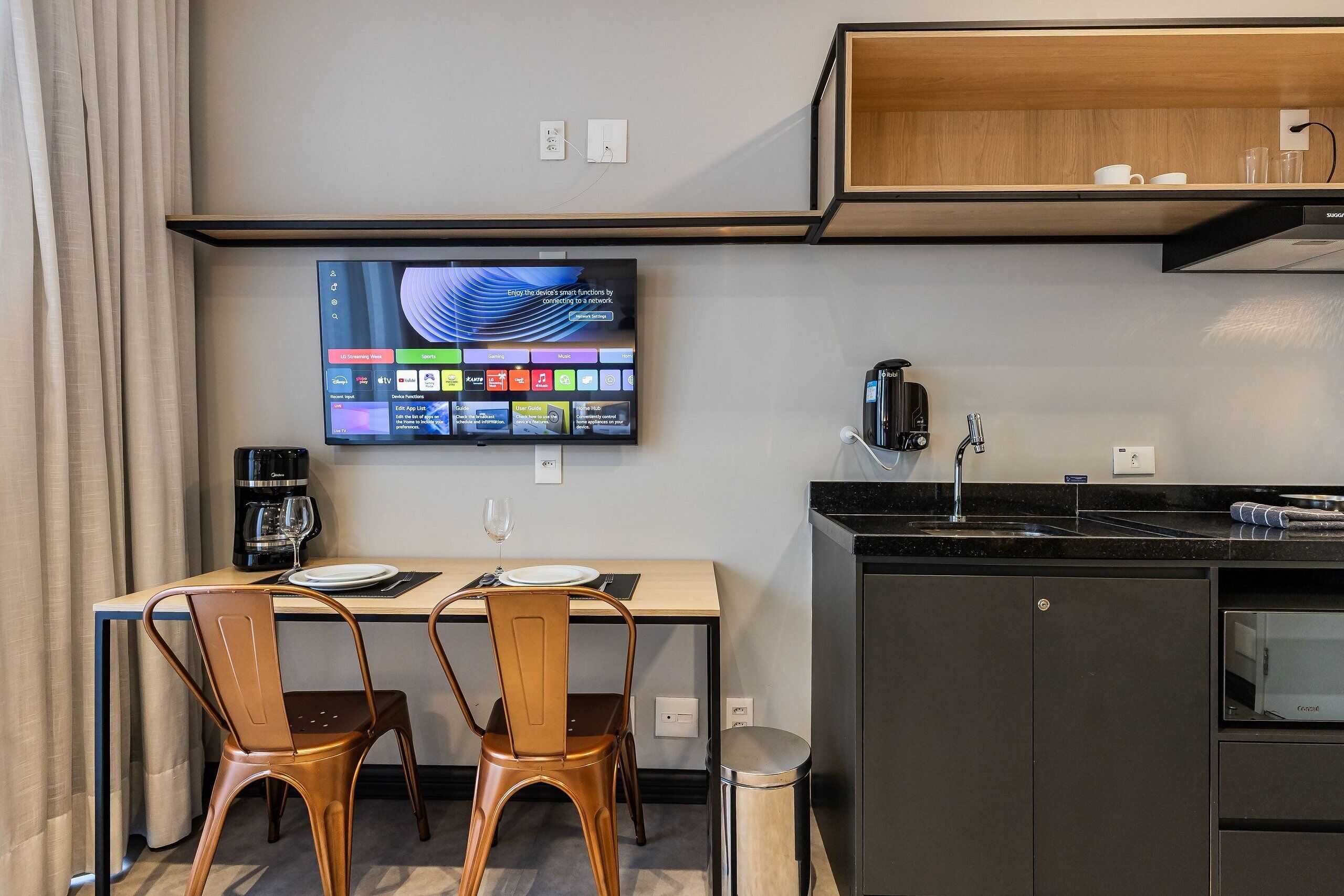 A modern kitchen with a flat-screen TV, a coffee maker, and a sink.
