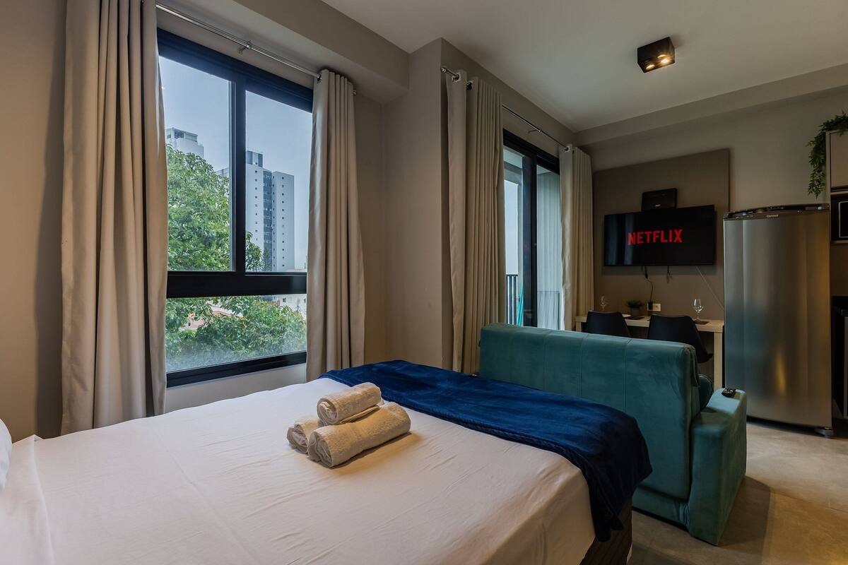 A hotel room with a bed, a desk, a TV, and a refrigerator.