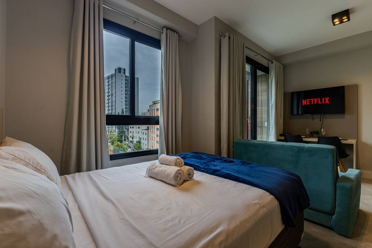 A hotel room with a bed, a desk, a TV, and a window with curtains.