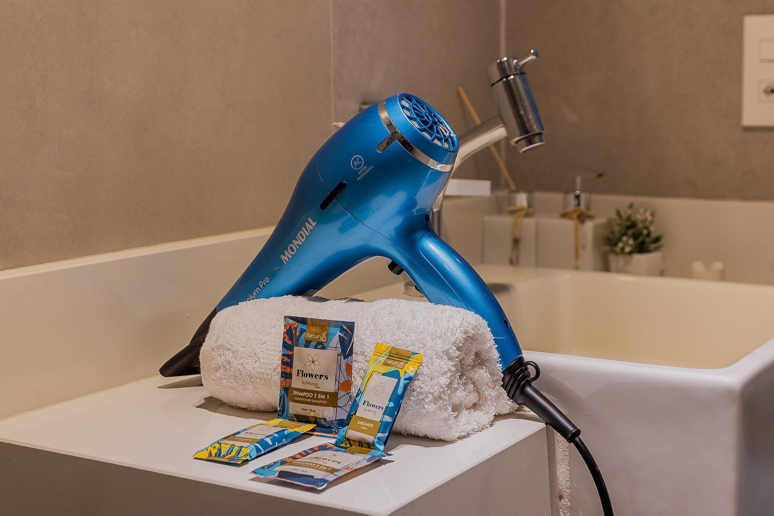 A blue hairdryer on a white shelf, a white towel, and two packets of shampoo.
