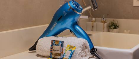 A blue hairdryer on a white shelf, a white towel, and two packets of shampoo.