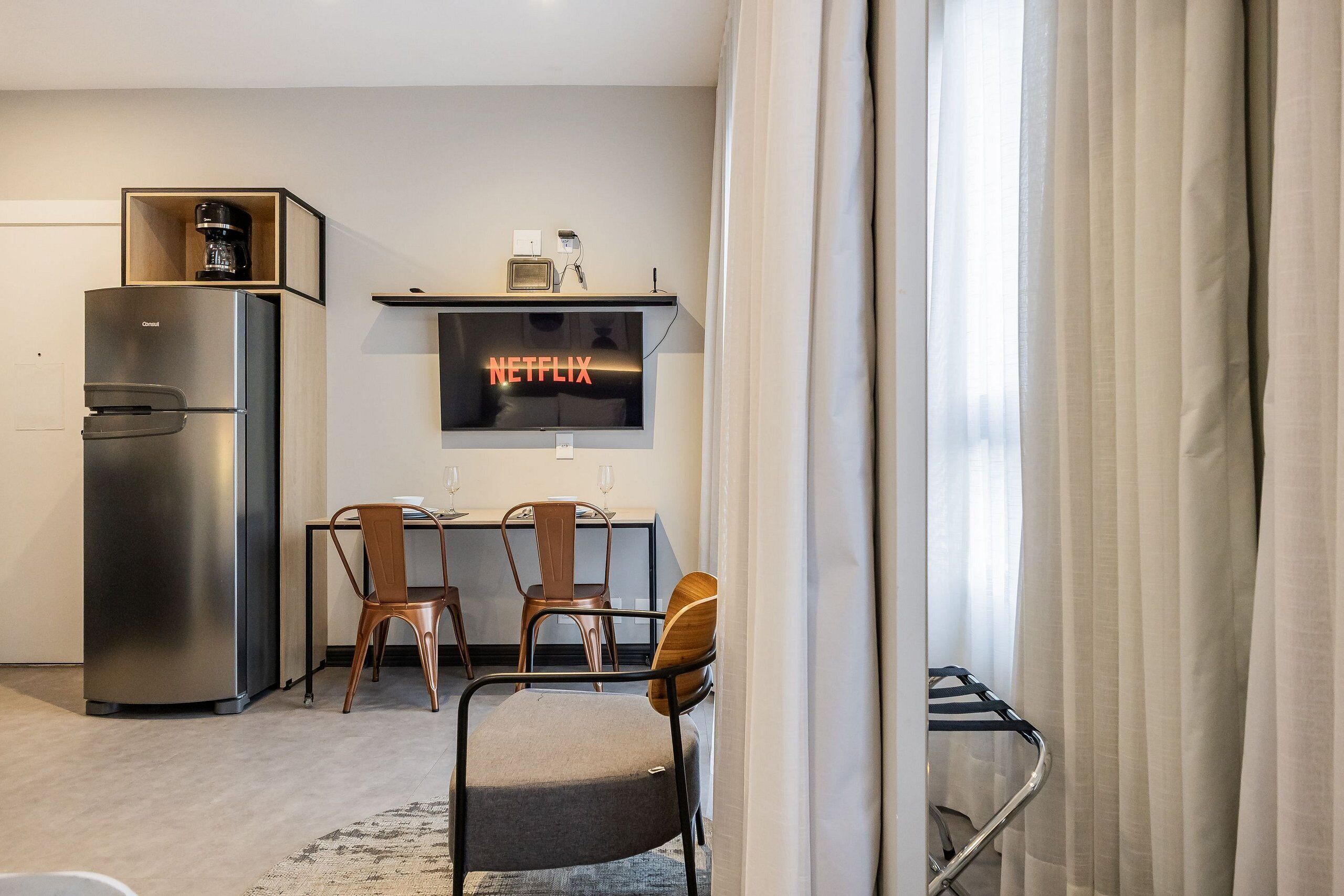 Una cucina moderna con frigorifero integrato, zona pranzo con due sedie, macchina del caffè e televisore a schermo piatto che mostra 'NETFLIX'.