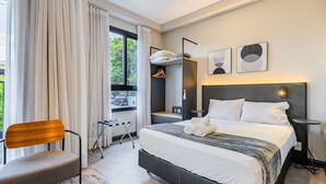 Ein modernes Hotelzimmer mit einem großen Bett, einem Sessel, einem Schreibtisch und einem Fenster mit Vorhängen.