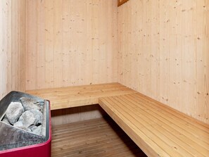 A sauna room with wooden benches and a metal container with rocks. - 12 Person Holiday Home in Pandrup (Pandrup)