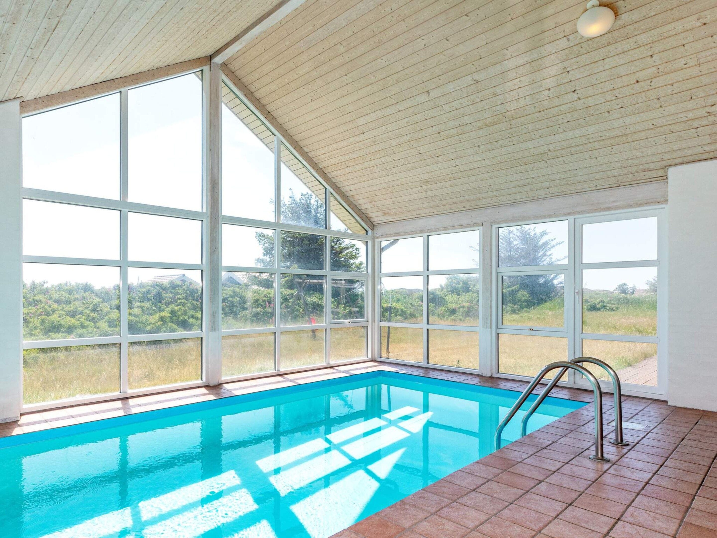 A swimming pool with a view of the outdoors through large windows.