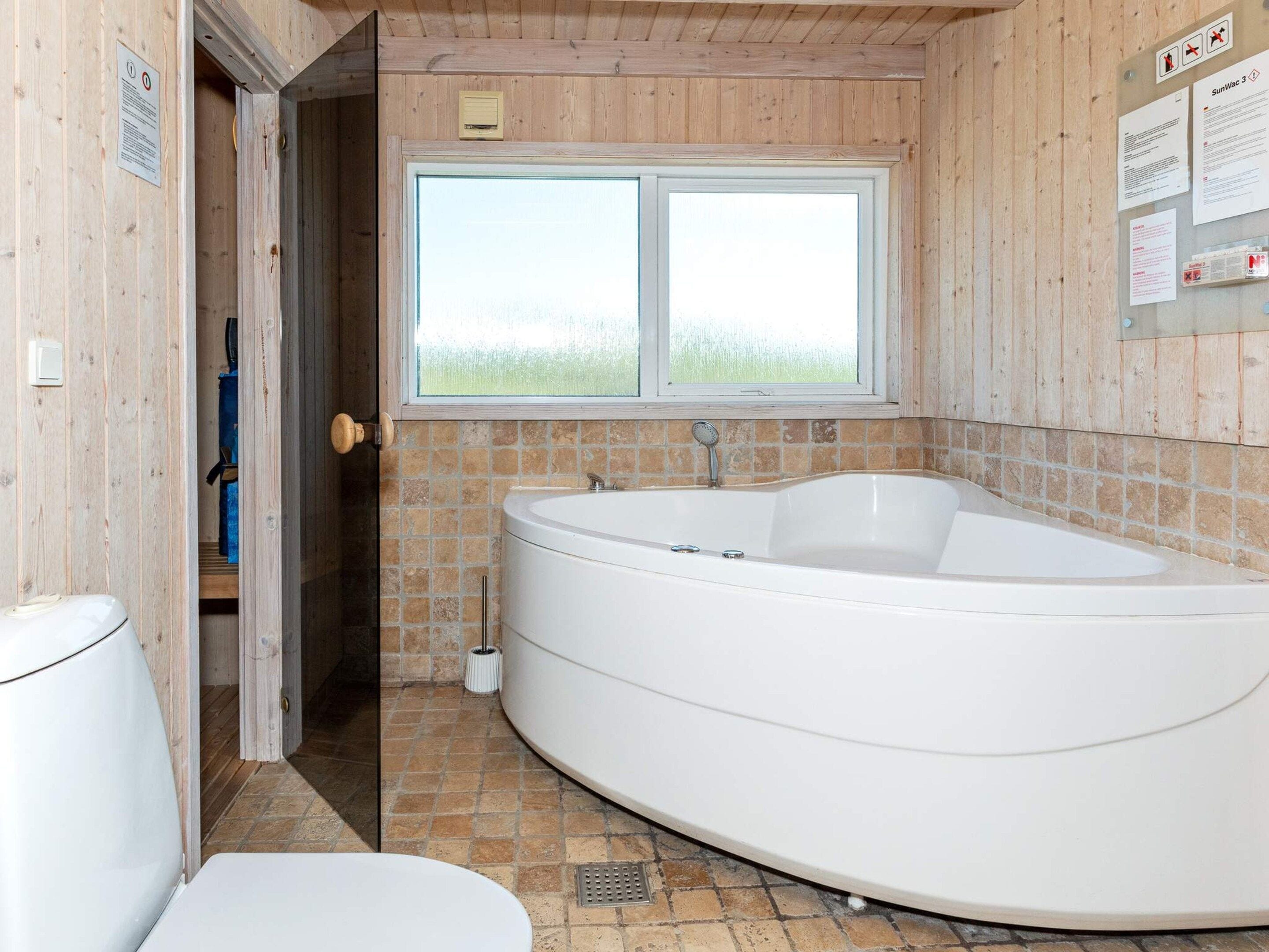 A bathroom with a large bathtub, a toilet, and a window providing a view of the outdoors.