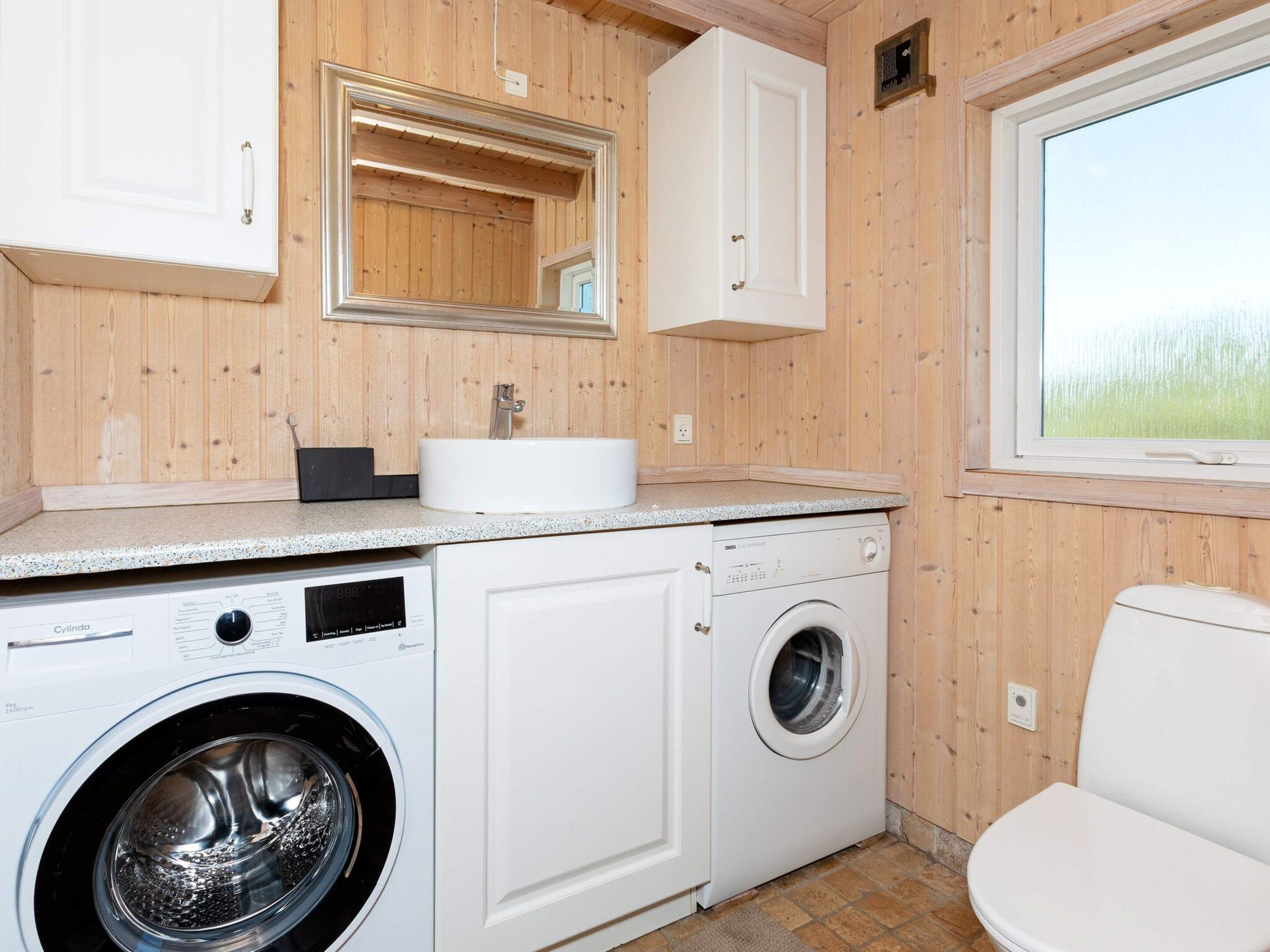 A compact laundry room with a washing machine, a dryer, a sink, and a mirror.