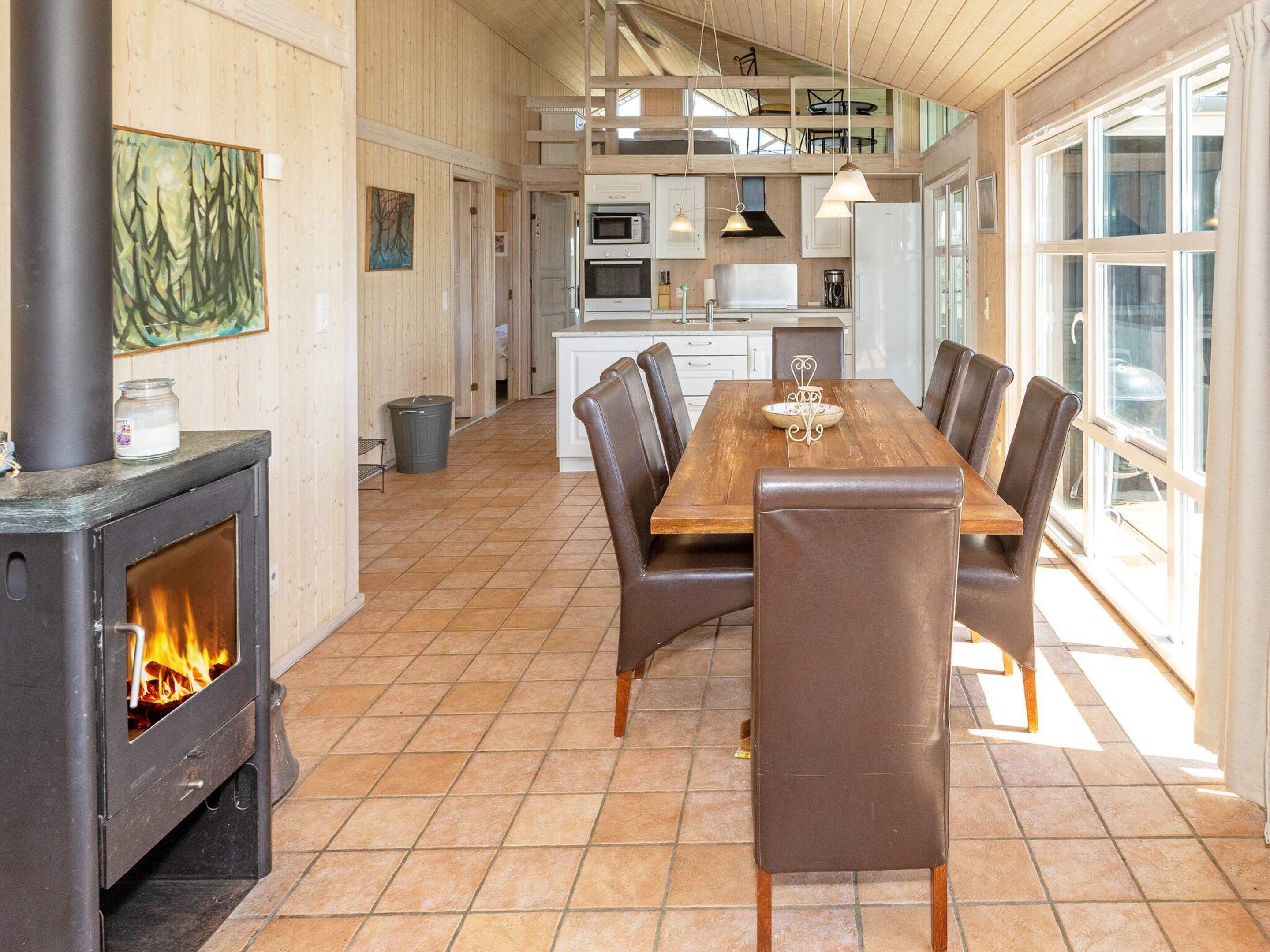 A spacious dining area with a wooden table and leather chairs, a kitchen in the background, and a wood-burning stove.