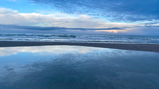 Una playa con superficie acuática reflectante y cielo nublado.