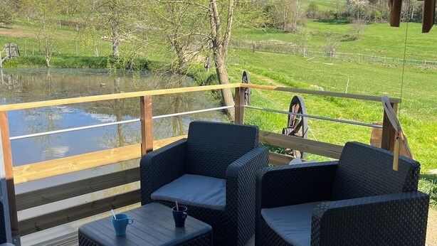 An outdoor deck with wicker furniture and a view of a lake and hills. - Cabane au Bord de L'eau (Saint-Pierre-Eynac)