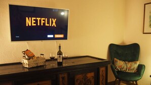 Ein Zimmer mit einem Fernseher, der das Netflix-Logo zeigt, einer Bar mit einer Weinflasche und einem grünen Polsterstuhl.