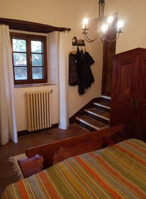 Een slaapkamer met een houten bed, een raam met gordijnen, een radiator, een trap en een kledingkast.