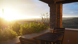 Ein Holztisch mit Stühlen auf einem Balkon mit Blick auf eine entfernte Landschaft und ein Gebäude.
