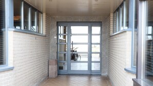 Un pasillo con suelo de baldosas, un vidrio con varios paneles y ventanas a ambos lados.