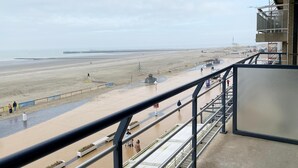 Vista a la playa desde un balcón con barandilla, una playa de arena y un muelle a lo lejos.