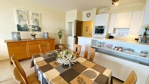 Una cocina moderna con armarios blancos, una isla central y una zona de comedor con mantel a cuadros.