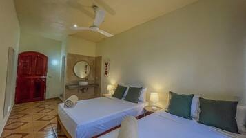 A hotel room with two beds, a ceiling fan, a bathroom with a sink and mirror, and a wooden door.