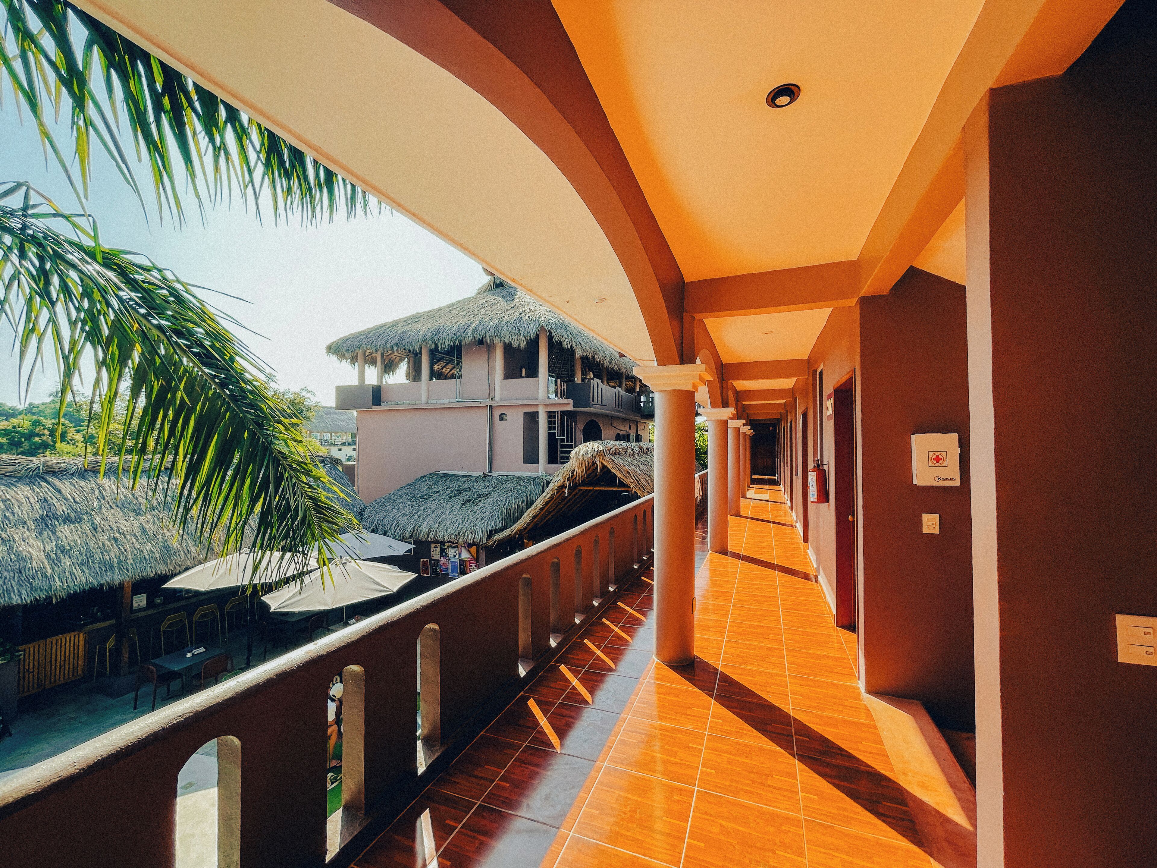 A corridor with a tiled floor, columns, and a view of a building with a thatched roof.