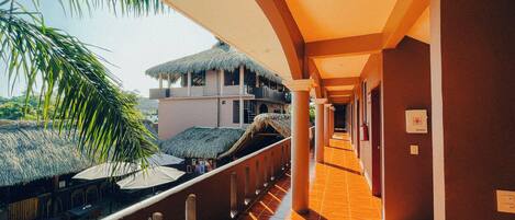 A corridor with a tiled floor, columns, and a view of a building with a thatched roof.