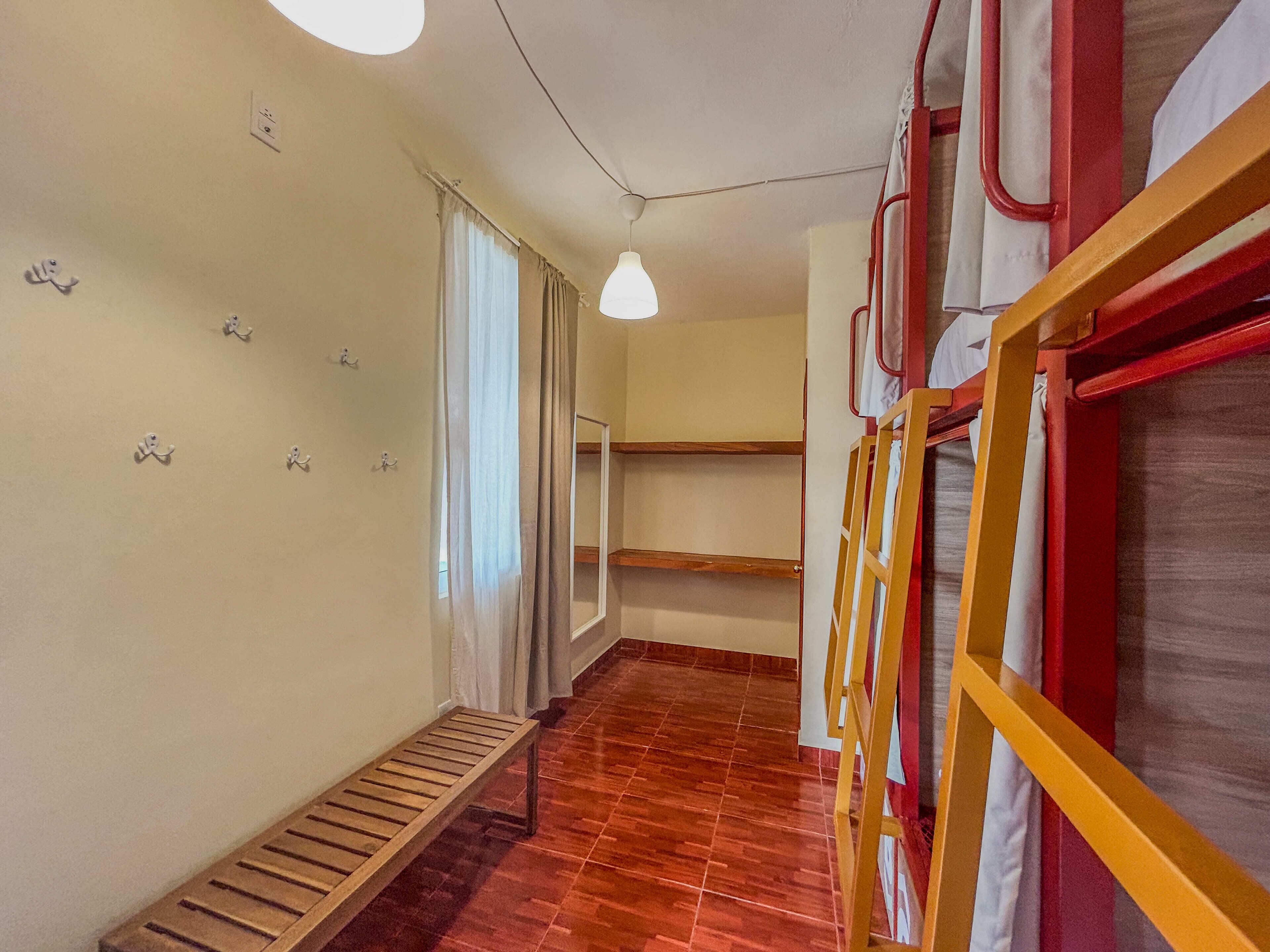 Un couloir avec des lits superposés, un banc en bois et un luminaire suspendu.